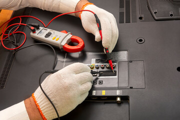 Engineer in service center repairs an LCD TV. Hands in white gloves use multimeter to measure the resistance, identify defect. Close-up, selective focus.
