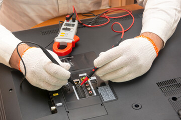 Engineer in TV repair service center looks for breakdown with multimeter, measures the resistance...