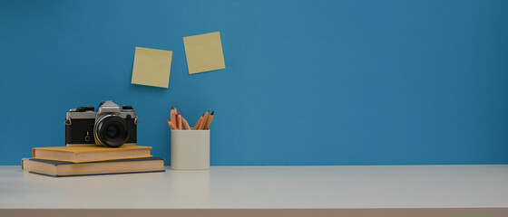 Worktable with camera, books, stationery and copy space on white desk with blue wall