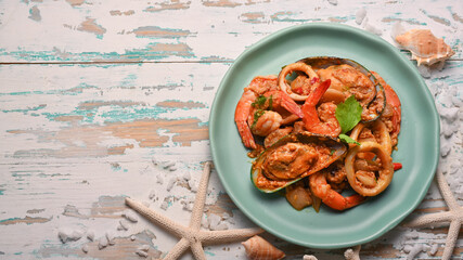 Thai food, seafood stir-fried curry powder on green ceramic plate on wooden table
