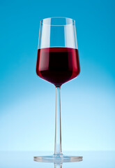 One glass of red wine on reflective surface. Studio photo isolated on blue background.