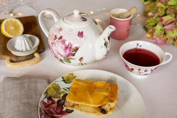 Teatime! Cute porcelain teapot and teacup  and a piece of decked apple pie, on an elegant table with white table cloth.