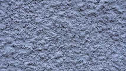 Dove-colored gray texuted plaster with a pronounced rough surface. Concrete wall of the house. Rough and uneven smears of cement on the wall. External construction finishing works.