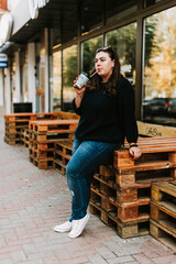 Portrait of a young adult girl with a Cup of coffee near a cafe in good autumn weather