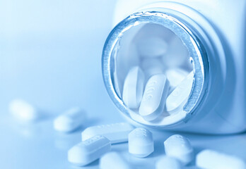 White medical pill and pill bottle on blue background.