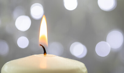 Close up of one burning candle with blurred Christmas light background