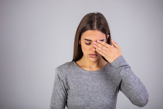 Woman suffering from strong eye pain against a gray background. Female has a pain in the eye. Healthcare concept. Having migraine. Upset woman suffering from strong eye pain.