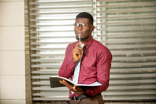 handsome business man standing with a register plus a pen in his hands while reflecting