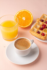 breakfast of waffles with honey orange juice and black coffee on a pink background.