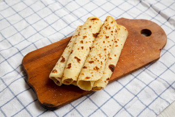 Homemade Norwegian Potato Flatbread (Lefse) with Butter and Sugar on a rustic wooden board on cloth, side view.