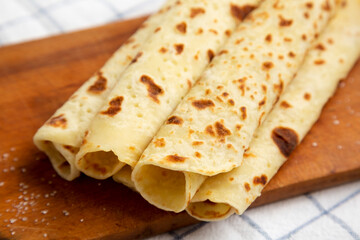Homemade Norwegian Potato Flatbread (Lefse) with Butter and Sugar on a rustic wooden board on cloth, side view. Close-up.