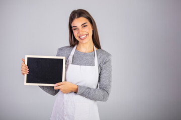 Beautiful Caucasian woman in barista apron holding empty blackboard sign studio shot - ready to insert text. Friendly smiling shop assistant holding blank chalkboard