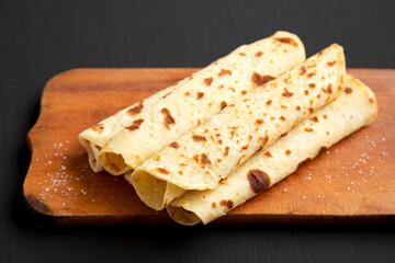 Homemade Norwegian Potato Flatbread (Lefse) with Butter and Sugar on a rustic wooden board on a black surface, side view. Close-up.