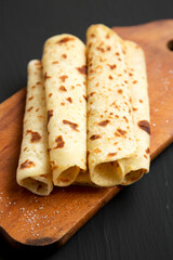Homemade Norwegian Potato Flatbread (Lefse) with Butter and Sugar on a rustic wooden board on a black surface, side view.