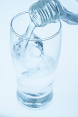 氷の入ったコップにペットボトルで水を注いでいるところで、コップの3分の1くらいまで水が入っているところ。