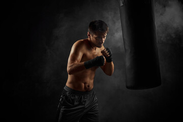 Fototapeta na wymiar Male boxer training defense and attacks in boxing bag on black background