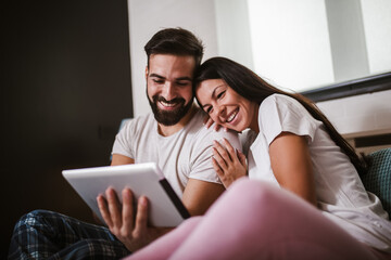 Smiling relaxed young couple using digital tablet in bed at home