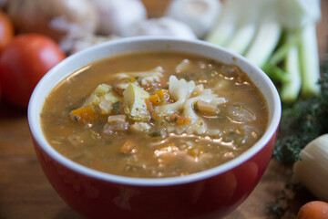 Minestrone soup, a typical thick vegetables soup, originally from Italy, served in a red bowl with Farfalle Pasta. 