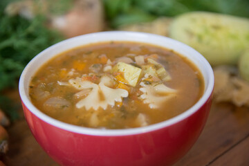 Minestrone soup, a typical thick vegetables soup, originally from Italy, served in a red bowl with Farfalle Pasta. 