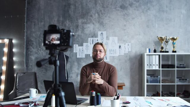 Young fashion vlogger is recording video vlog about design of clothes. Stream of talented stylist from his workplace in modern loft.