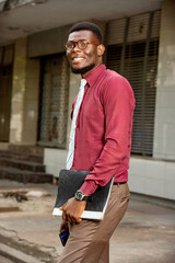 handsome young african walking on the street while holding a not