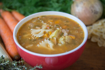 Minestrone soup, a typical thick vegetables soup, originally from Italy, served in a red bowl with Farfalle Pasta. 