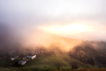 Sonnenuntergang auf der Alm wo ein Bauernhof zu sehen ist und alles ist von Nebel umgeben