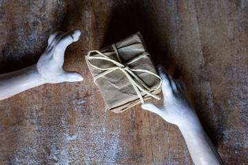 Doll hands with ecological wrapped gift. Top view on wooden table. Concept of sustainability