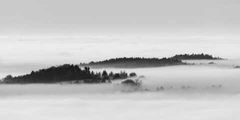 Durch den Nebel im Thal treten Spitzen von Bäumen hervor, auch ein Haus ist zu erkennen