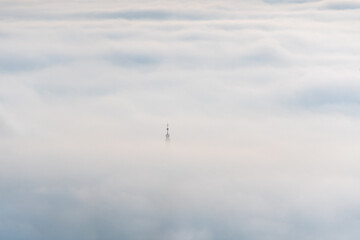 Eine Kirchturmspitze ragt aus dem Nebelmeer hervor im Morgenlicht
