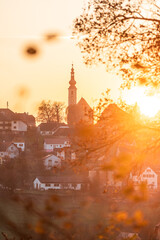 Die Dorfkirche ist Mittig auf einer Anh&ouml;he zu sehen, alles ist in warmes Sonnenuntergangslicht geh&uuml;llt, auch andere H&auml;user und &Auml;ste sind zu sehen