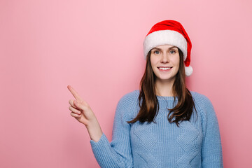 Lovely young woman in Christmas red hat points fore finger right, suggests going this direction,...