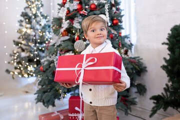 cute little boy with Christmas gift box near Christmas trees with lights. Merry Christmas and Happy Holidays