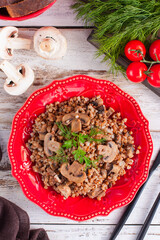 Cooked buckwheat porridge with fried mushrooms in a red plate, selective focus