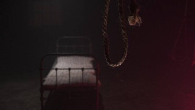 scary noose gallows for execution swings in dark against background of white metall bed in dark hospital or hangar sinister. Horror movie concept. bed with old mattress for corpse after hanging.