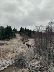first snowfall among trees and winding river in hilly terrain
