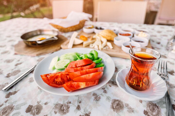 Fototapeta na wymiar Traditional Turkish glass with strong tea, vegetables and other snacks for a rich middle eastern Breakfast in the outdoor restaurant