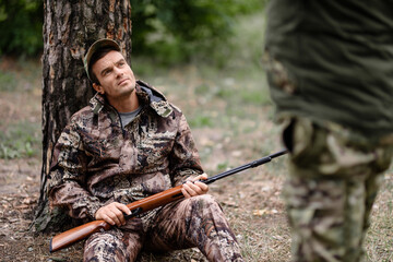 Hunter with Rifle Has Rest Men Hunting in Forest.
