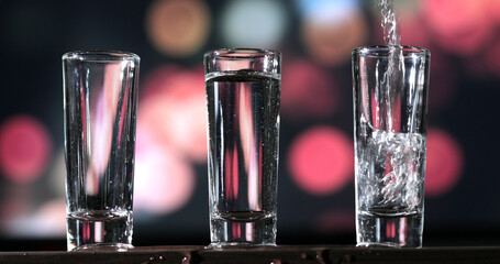 Bartender pouring up tequila into three shots glasses.