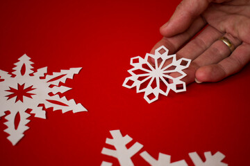 Female hand holding white paper snowflake on red background