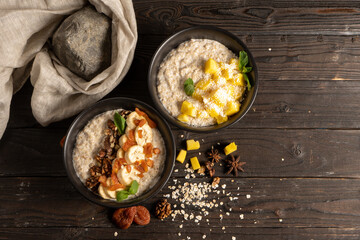 Oatmeal with fresh mango pieces, banana, dried apricots and walnuts, cooked in milk and decorated with mint chanterelles. Two servings of classic vegetarian breakfast on a wooden kitchen table.