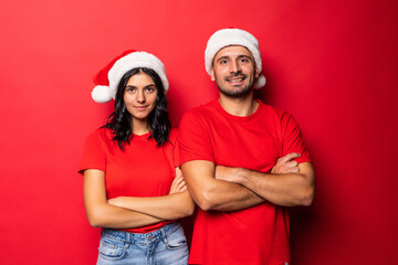 Cheerful young couple in Santa Claus hats together isolated over red background