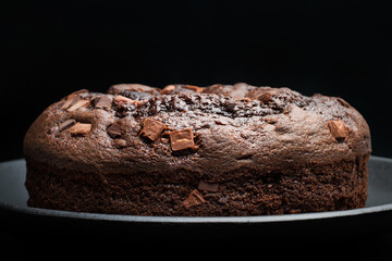 Bizcocho de chocolate redondo sobre un plato oscuro sobre un fondo negro liso y aislado. Vista de frente. Copy space