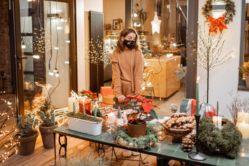 Lonely woman in facial mask during the New Year holidays at home on the beautifully decorated terrace. Concept of quarantine and self-isolation during the epidemic on holidays