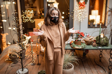 Portrait of a sad woman in facial mask during the New Year holidays at home on the beautifully decorated terrace. Concept of quarantine and self-isolation during the epidemic on holidays