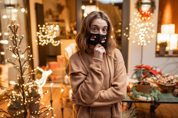 Portrait of a sad woman in facial mask during the New Year holidays at home on the beautifully decorated terrace. Concept of quarantine and self-isolation during the epidemic on holidays