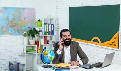 brutal bearded man work in classroom and hols smartphone. prepare for online exam. college lecturer on lesson. back to school. formal education. conversation. happy mature teacher speak on phone © be free