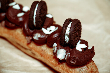 Eclair decorated with chocolate cream and cookies on parchment paper
