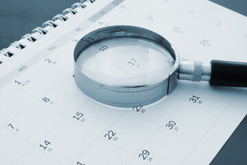 Magnifying glass on calendar close up. Review year events concept.