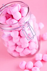 Glass jar filled with pink candy. Studio photo isolated on pink background. Selective focus on object.